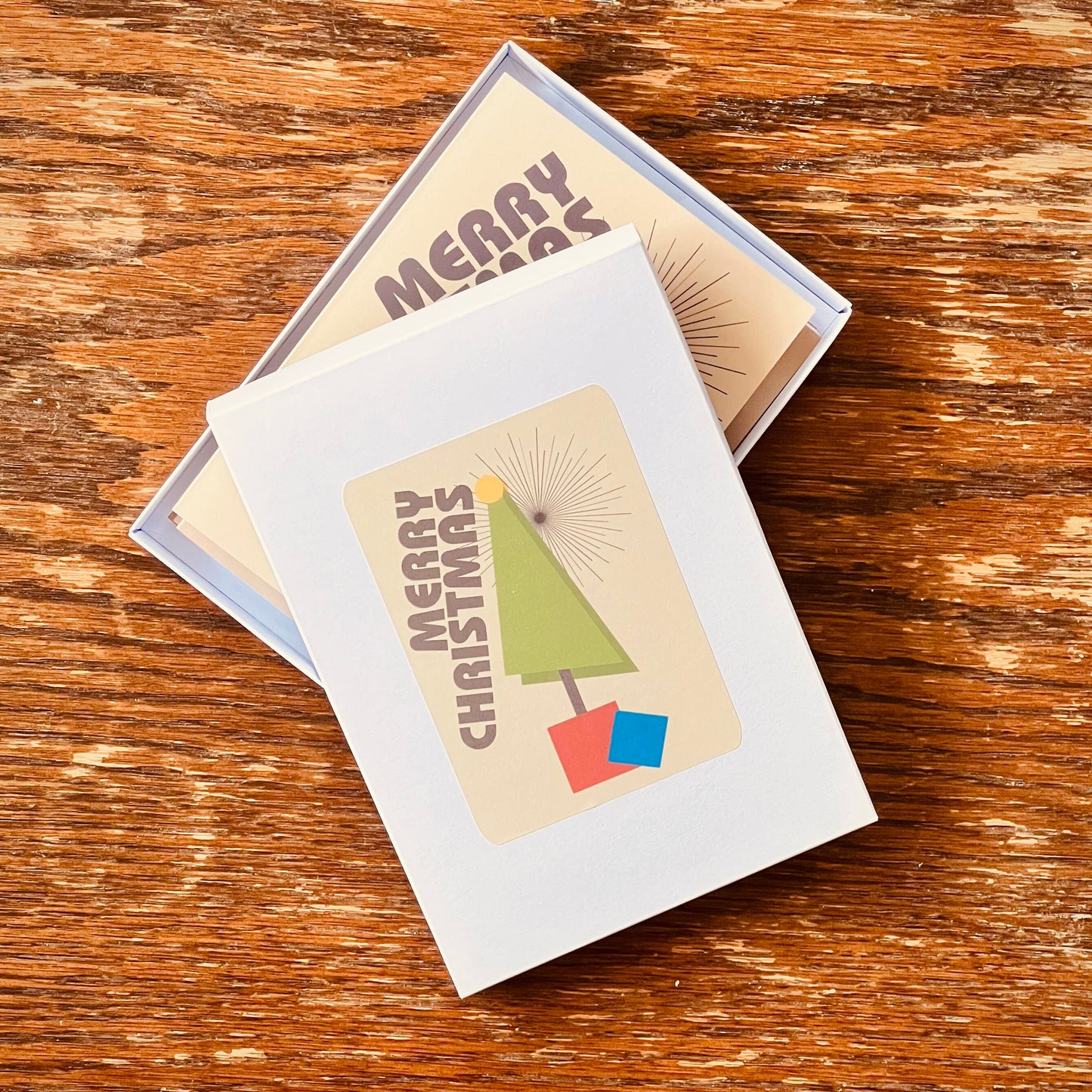 A box of Christmas cards. The design is a geometric tree in primary colours with the word Merry Christmas positioned diagonally along the side.