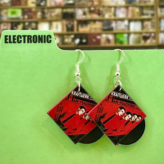 A pair of earrings in a record shop setting hanging on a category divider with the category &#39;Electronic&#39;. The cover artwork is Man Machine by Kraftwerk. The earrings are designed to look like an album with the vinyl peeking out.