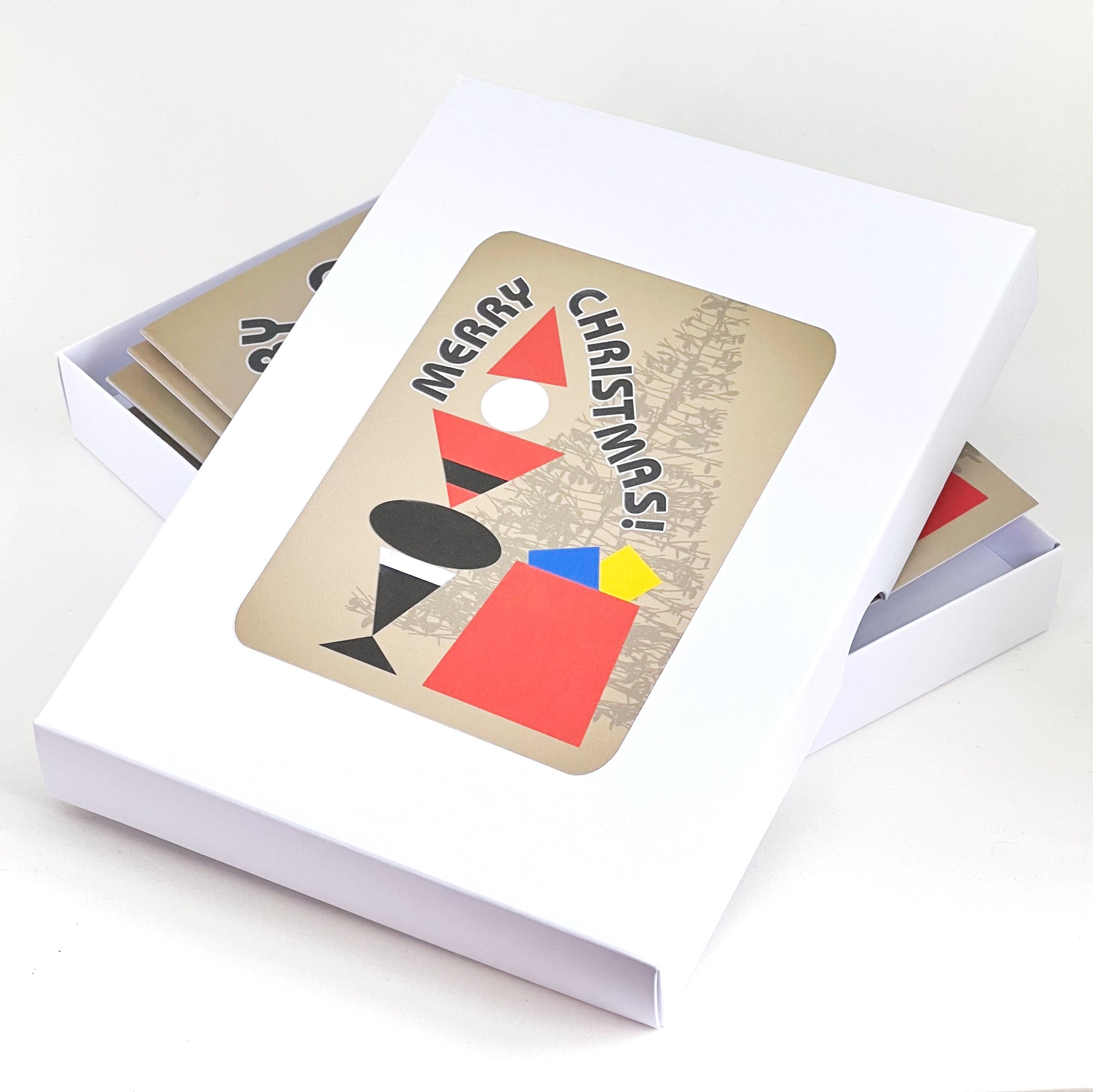 A box of Christmas cards. The design is a geometric figure representing Father Christmas in red and black, standing next to a red sack with presents and Christmas tree in the background. The words Merry Christmas flow around the figure.