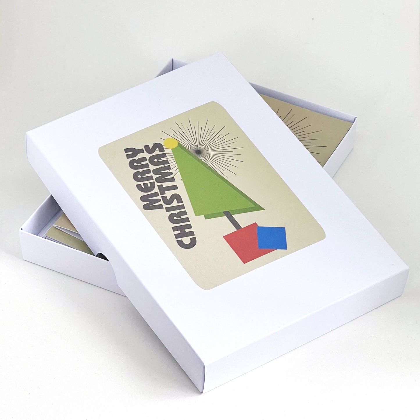 A box of Christmas cards. The design is a geometric tree in primary colours with the word Merry Christmas positioned diagonally along the side.