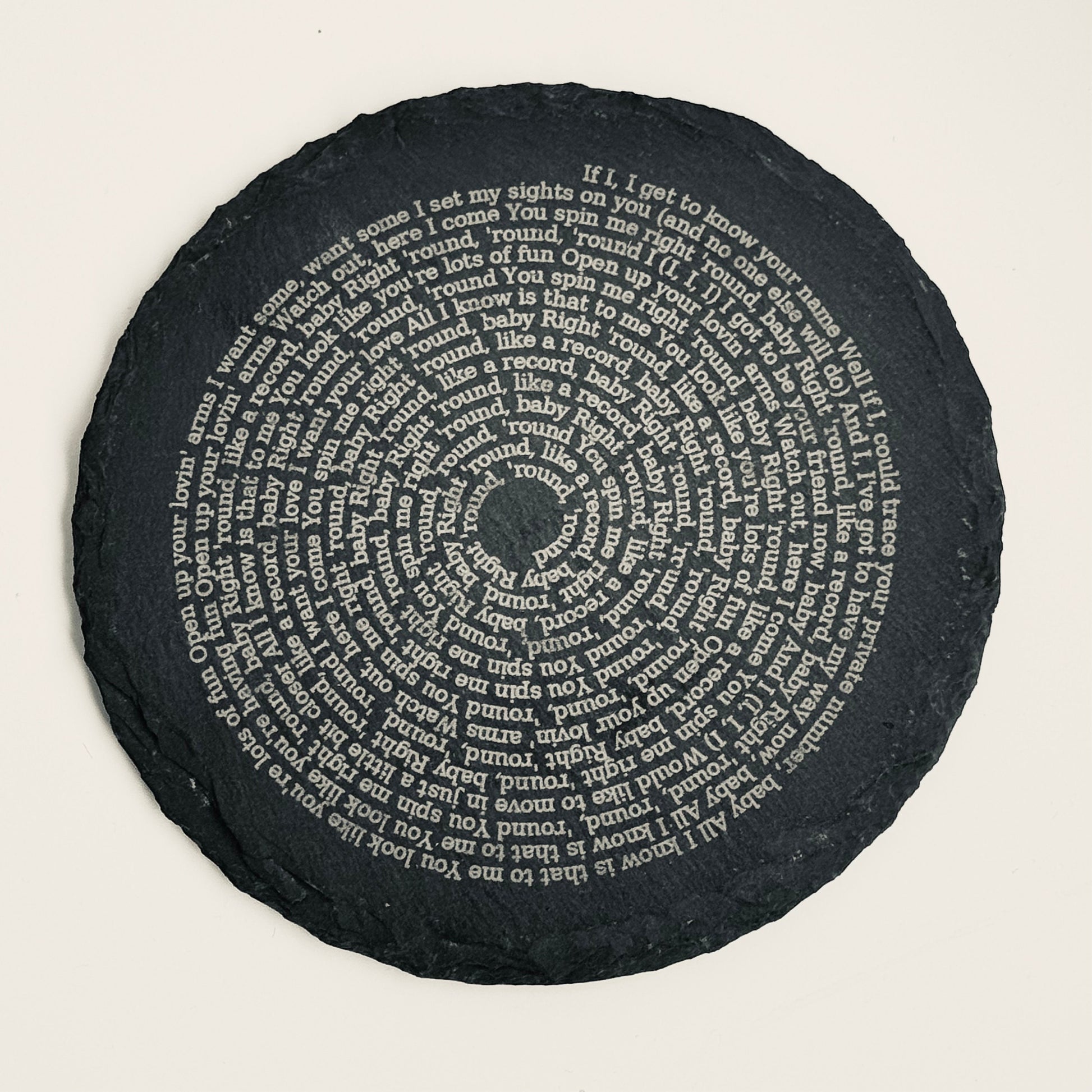 A slate coaster with the lyrics of ‘You Spin Me Round’ engraved on the surface.